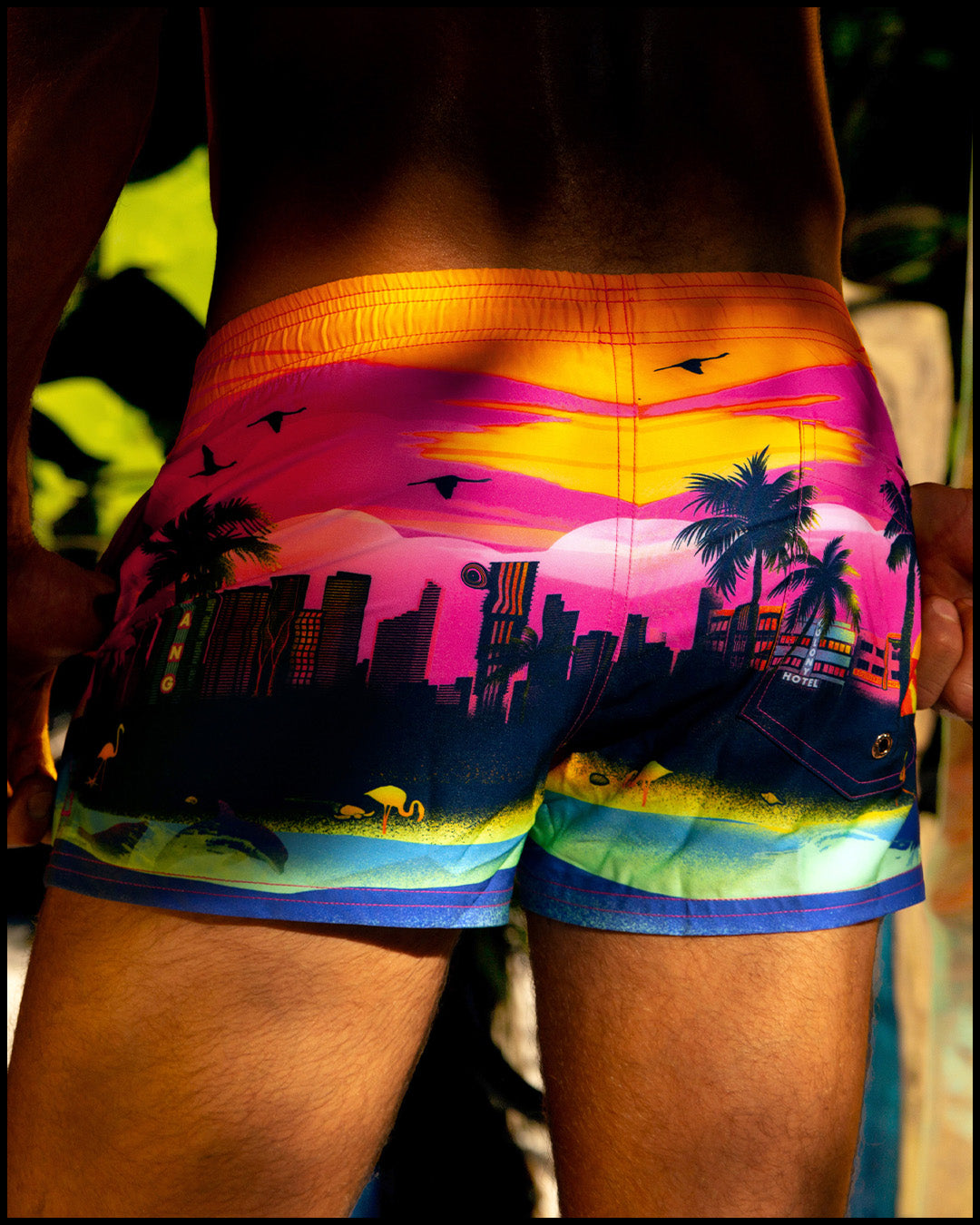 Male model pictured beachside, wearing the men’s UNDER A NEON SKY Mini Shorts from BANG! Clothes is the official brand for men’s swimwear brand.