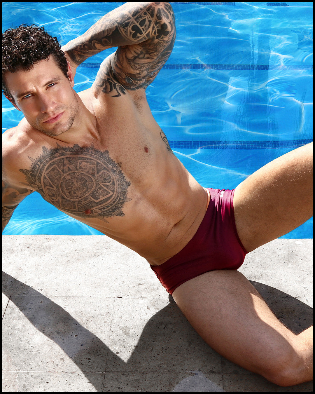 Male model lounging poolside wearing VERY BERRY men’s Brazilian Swim Sunga made by the Bang! Miami’s official brand of men's swimwear.