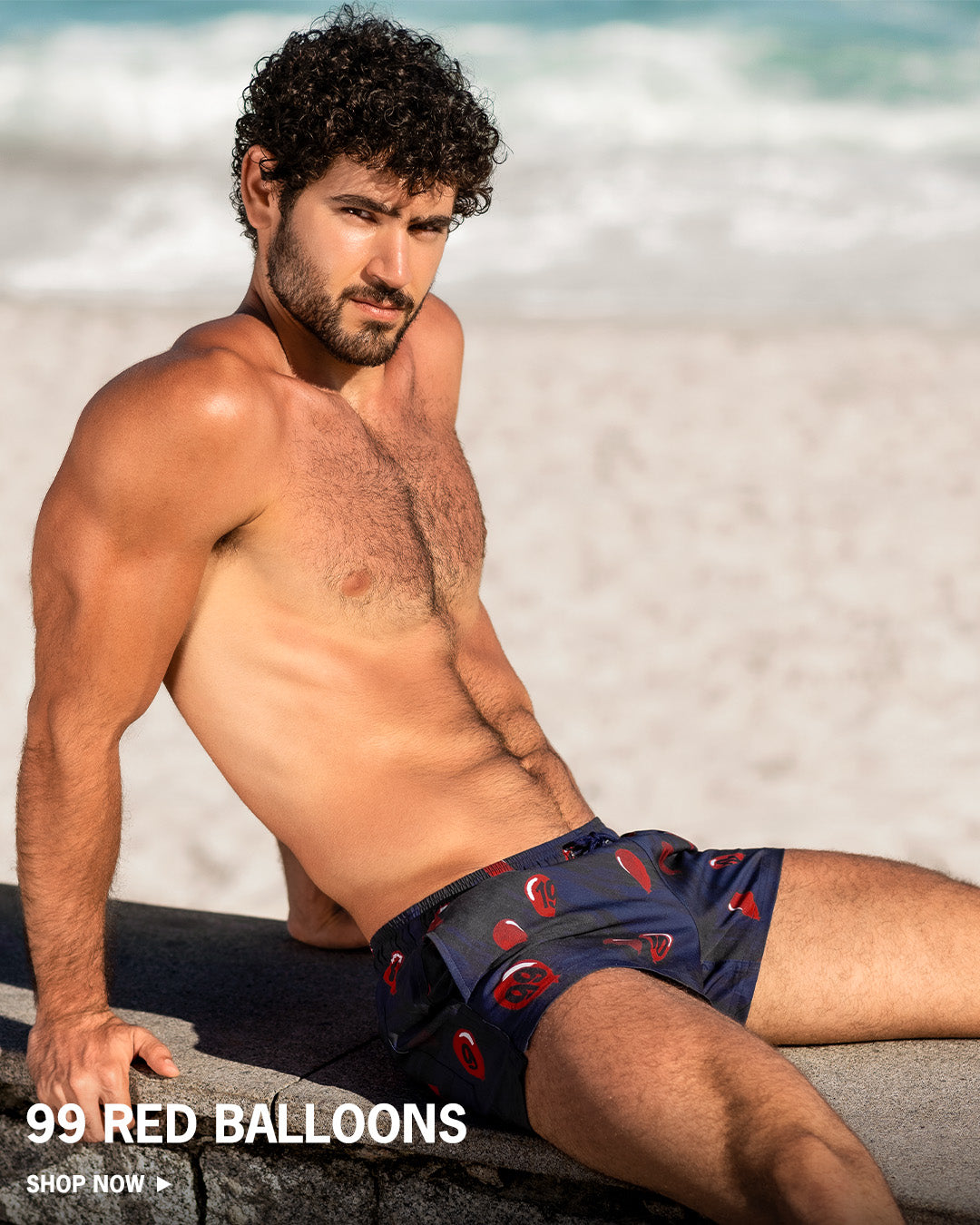 Man wearing navy swim trunks with red balloon pattern on a beach