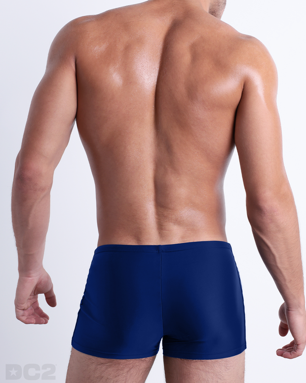 Back view of a male model wearing the BLUE BY THE OCEAN men’s swim trunks by BANG! Miami in a solid vibrant blue color.