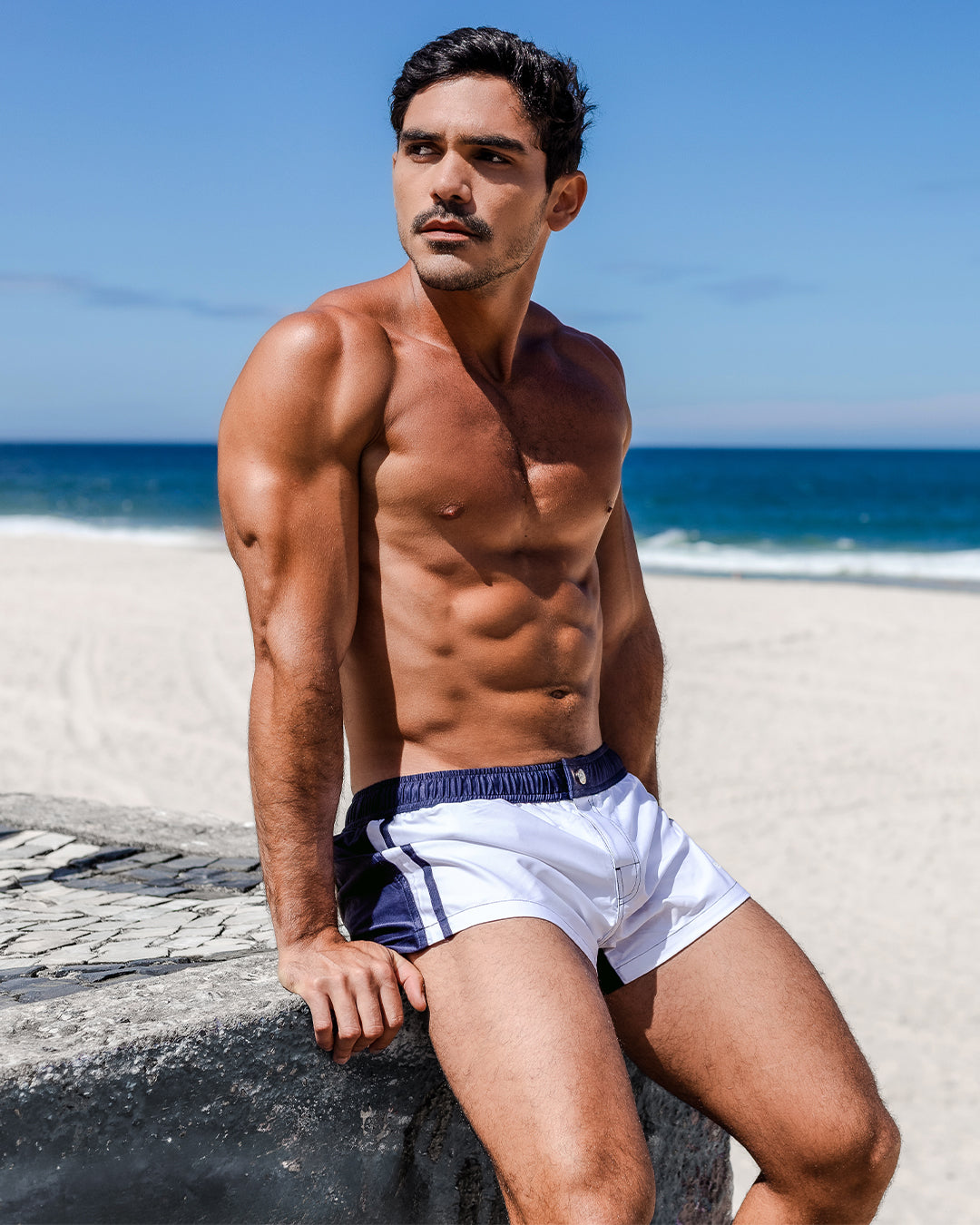 Men’s white and navy swim mini shorts with elastic waistband, worn at the beach by model, featuring a short cut, tailored fit, and quick-dry fabric.