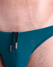 Close-up view of the CHIC TEAL men’s drawstring briefs showing black cord with custom branded metallic silver cord ends, and matching custom eyelet trims in silver.