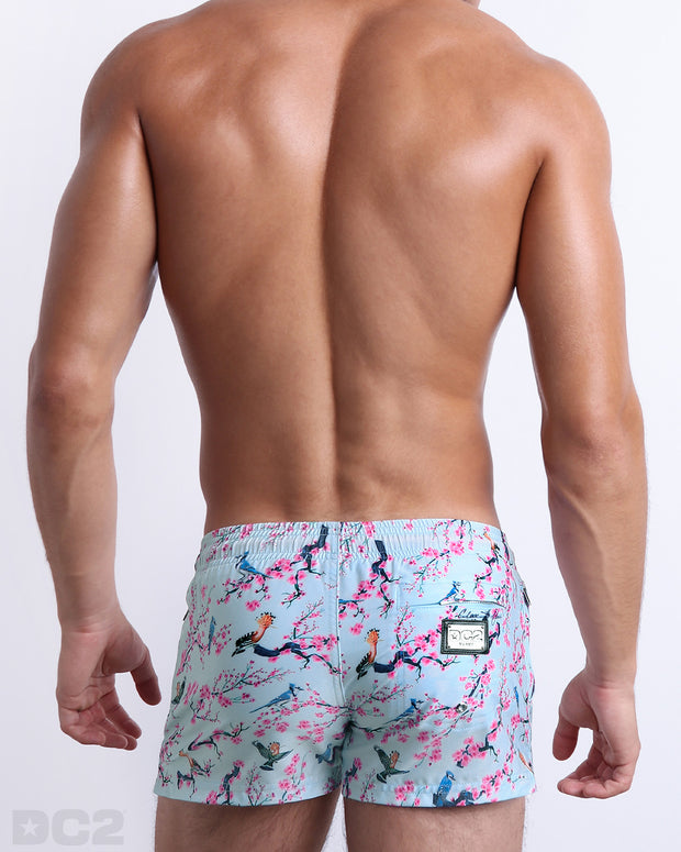 Back view of the CLOSE TO YOU beach Poolside Shorts in a light blue color with an exotic birds print, complete with a back pocket, designed by DC2.