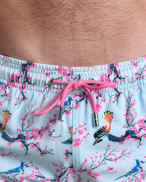 Close-up view of the CLOSE TO YOU men’s Poolside Shorts with pink flowers and branches birds print, showing custom branded silver zippered pockets.