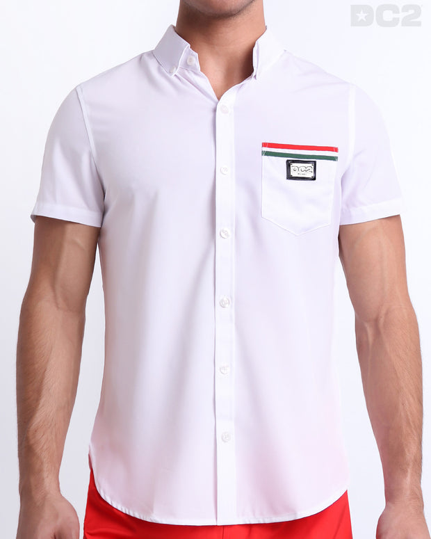 Front view of a sexy male model wearing FORZA WHITE men’s short-sleeve stretch shirt in a white color with red and green colored stripes on the from left pocket for men. This premium quality button-up top is by DC2, a men’s beachwear brand from Miami.