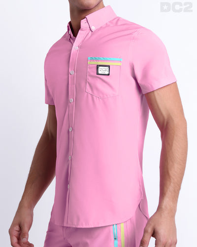 Side view of a masculine model wearing the men’s PADAM PINK Summer button-down shirt in a solid pink color with stylish pastel yellow and aqua blue colored stripes. This high-quality shirt is by DC2, a men’s beachwear brand from Miami.