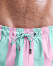 Close-up view of inseam and details of THE KEN (MALIBU EDITION) swimsuit for men, with light aqua green color cord and custom branded golden cord-ends, and matching custom eyelet trims in gold.