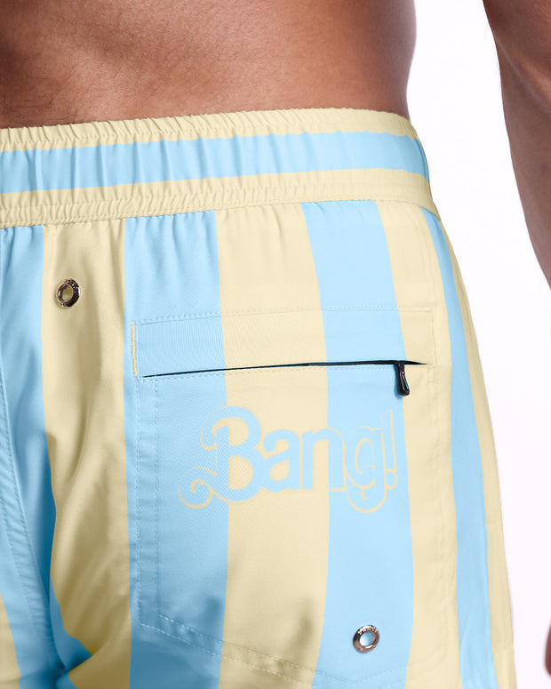Back view of a male model wearing men’s THE KEN (MIAMI EDITION) beach Mini Shorts swimsuit by BANG! Clothes in Miami, featuring yellow and light blue colored stripes. Complete with a zippered back pocket.