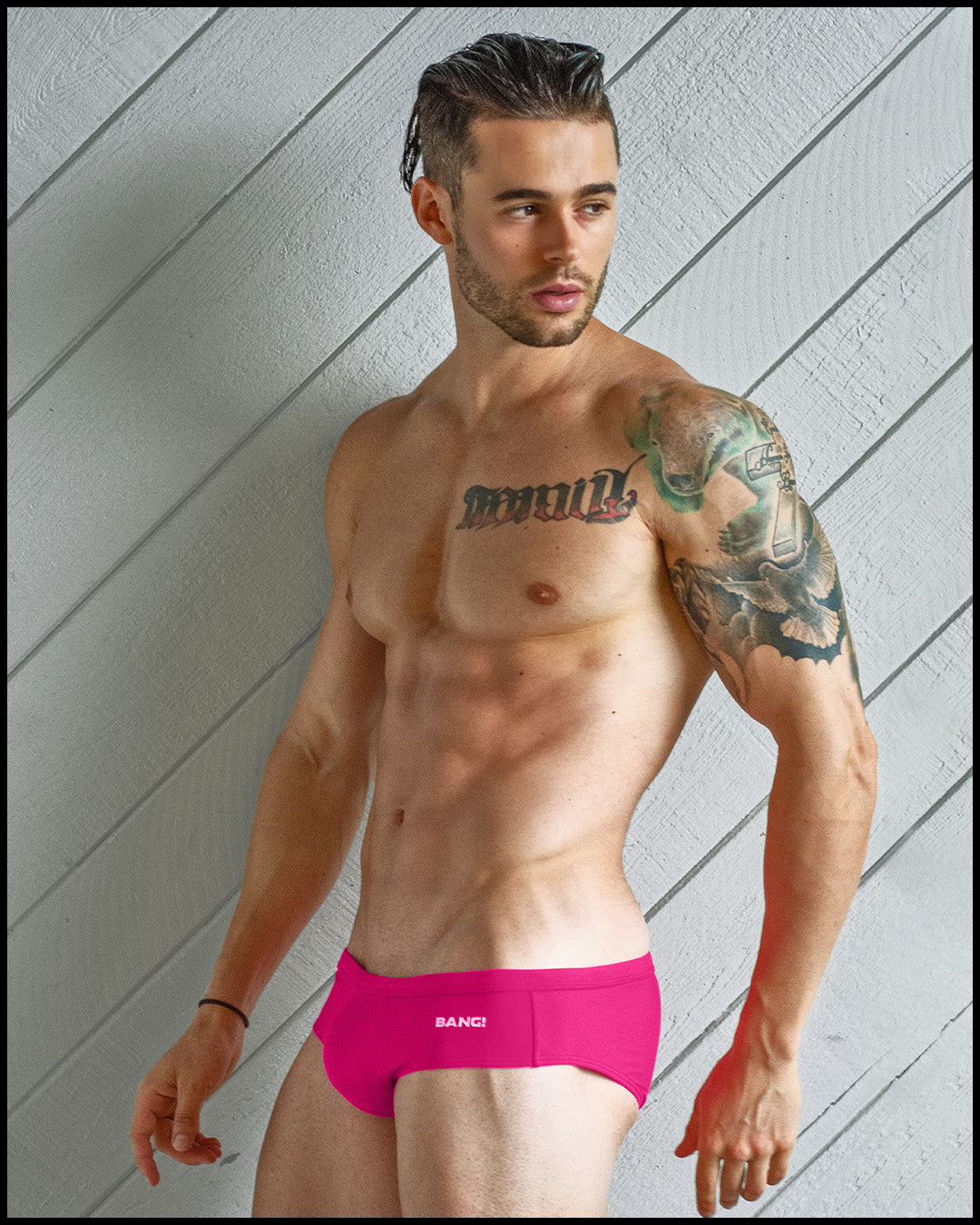 Side view of a masculine model wearing men’s swim European bikini in bright hot pink color with official logo of BANG! Brand in white.