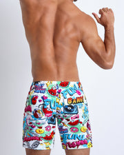 Back view of a sexy male model wearing men’s swimwear made by the Bang! official brand of men's beachwear.Back side of the BANG ONE men’s mid-length beach shorts features fun and energetic comics-style graphics in bold colors, with a BANG! illustration  by BANG! Clothes.