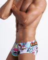 Side view of an in-shape men's torso wearing a sexy Brazilian sunga men swimsuit featuring cool graffiti print in bold colors with a prominent BANG! sign.