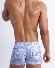 Back view of male model wearing the SPLASH  beach shorts for men by BANG! Miami in white and blue color with graphics of water and wet letters.
