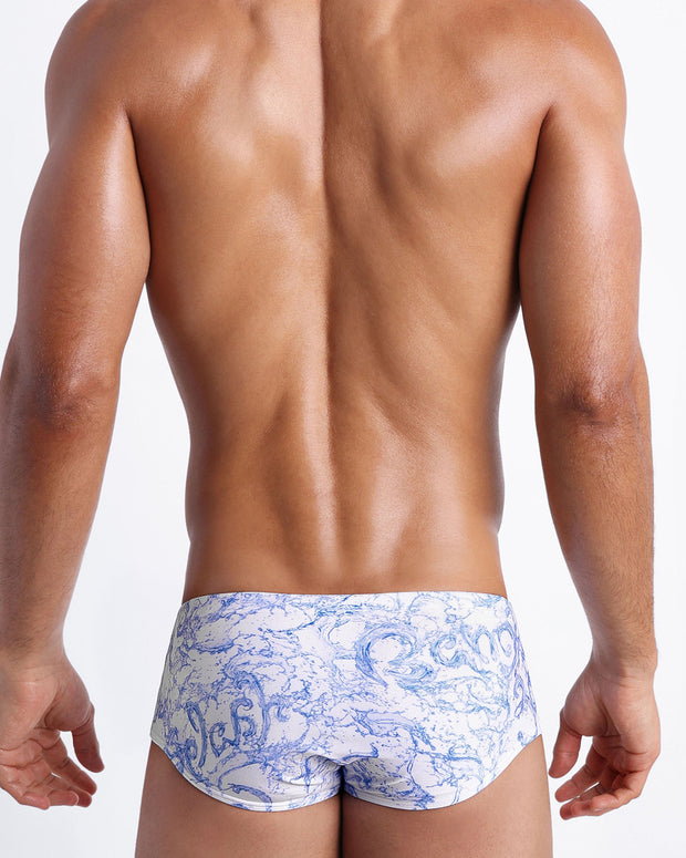 Back view of male model wearing the SPLASH  beach sungas for men by BANG! Miami in white and blue color with graphics of water and wet letters.
