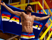 Male model at the beach wearing the STRIPE’A’POSE Show Shorts and holding the matching light-weight & portable beach towel. 