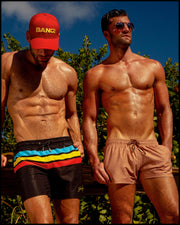 Male models at the beach in their BANG! Clothes men’s swimwear. The model on the left is wearing the BIONIC STRIPES Resort Shorts. The model on the right is wearing the TOP TAN Show Shorts.