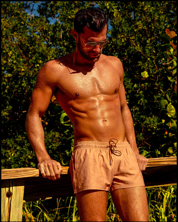 Male model at the beach wearing the TOP TAN Show Shorts by BANG! Clothes the official men’s swimwear brand based in Miami, FL.