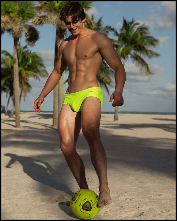 Male model in an outdoors setting wearing the ULTRA NEON Brazilian Swim Sunga by BANG! Clothes is a men’s swimwear brand based in Miami, FL. 