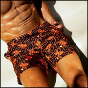 Male model sitting wearing the TIGER HEARTS swimwear shorts for men featuring Brown with Orange Tigers pop art by BANG! Clothes.