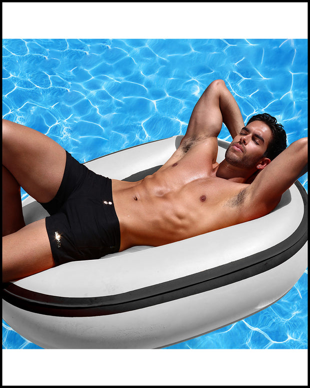 Male model in a pool wearing the DARK KIGHT a solid black Beach Shorts by BANG! Clothes.