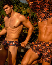 Two men are modeling BANG! Clothes' latest men's swimwear collection at the beach. One is wearing a Brazilian Swim Sunga, while the other is sporting Tailored Shorts with a matching Tank Top.