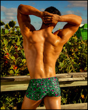Male model at the beach wearing swim trunks for men in teal with pink and black animal print by the Bang! Clothes brand of men's beachwear.