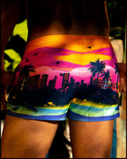 Male model pictured beachside, wearing the men’s UNDER A NEON SKY Mini Shorts from BANG! Clothes is the official brand for men’s swimwear brand.
