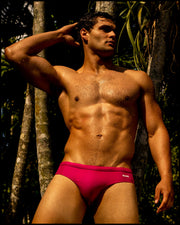 Male model wearing the CONFESS MAGENTA Swim Brief a bright magenta pink color. The swimsuit is by BANG! Clothes, the official brand of men’s high-quality beachwear.
