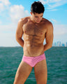 Male model posing outdoors with the Miami skyline in the background in his vibrant PINKTYQUE Swim Brief, a bright pink design by DC2, a men’s beachwear brand from Miami.