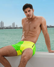 Male model is wearing the SINGLE BILINGUAL (NEON YELLOW/GREEN) Beach Shorts, from BANG! a men’s beachwear brand based in Miami.