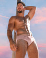 Male model outdoors wearing the NAKED PINK Swim Brief, a light pink color by the Bang! Menswear brand from Miami.