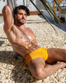 Male model wearing the AMBER SAND Swim Sunga, a solid vibrant sunny yellow color by DC2, a men's beachwear brand from Miami.