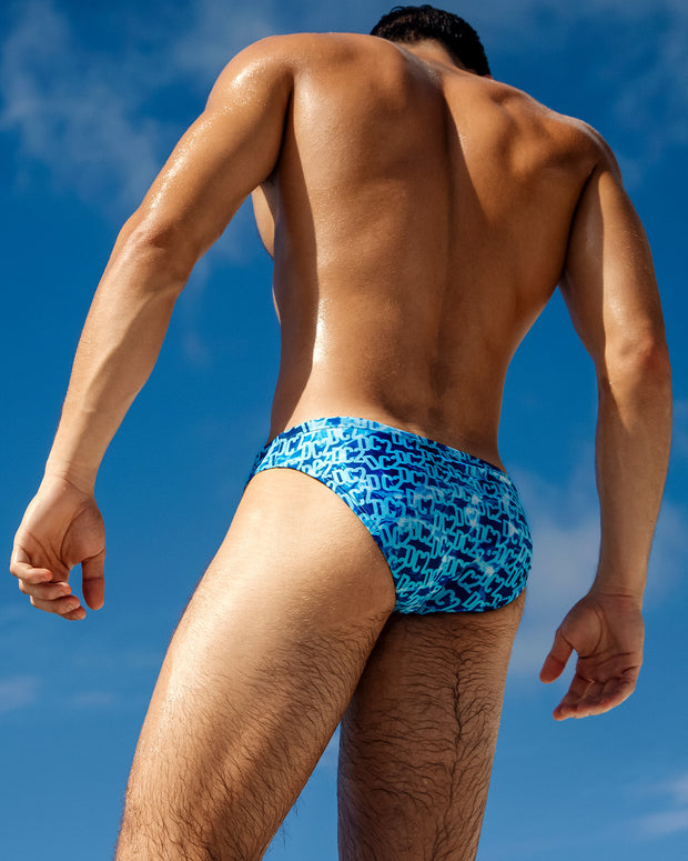 Back view of a model wearing DC2 Miami WET Swim Mini Briefs, showcasing the bold blue gradient design with DC2 branding.