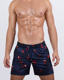A male model wearing the 99 RED BALLOONS Resort Shorts by DC2 Miami. These stylish shorts feature a deep navy base with striking red balloon prints, a drawstring fastening, and gold-tone aglets.