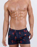 Frontal view of a male model wearing the 99 RED BALLOONS Show Shorts by BANG! Miami. These stylish, quad-friendly beach shorts feature a deep navy blue base adorned with scattered red balloon prints, an elasticated drawstring waistband with metallic tips, and a contoured fit designed for beach, resort, and summer wear.