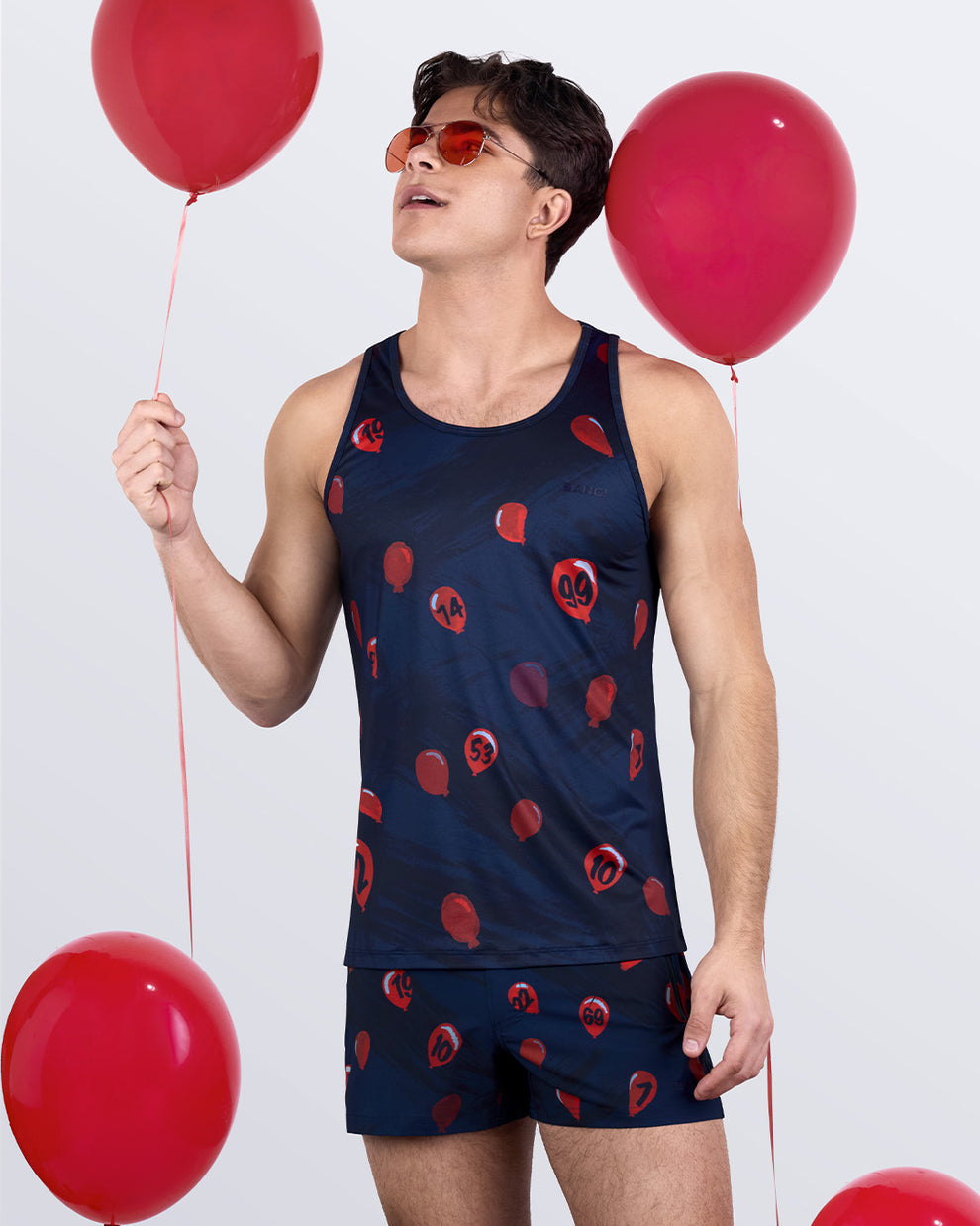 Model wearing 99 RED BALLOONS tank top and shorts set, holding red balloons – fun and festive men’s activewear outfit by BANG!® Miami
