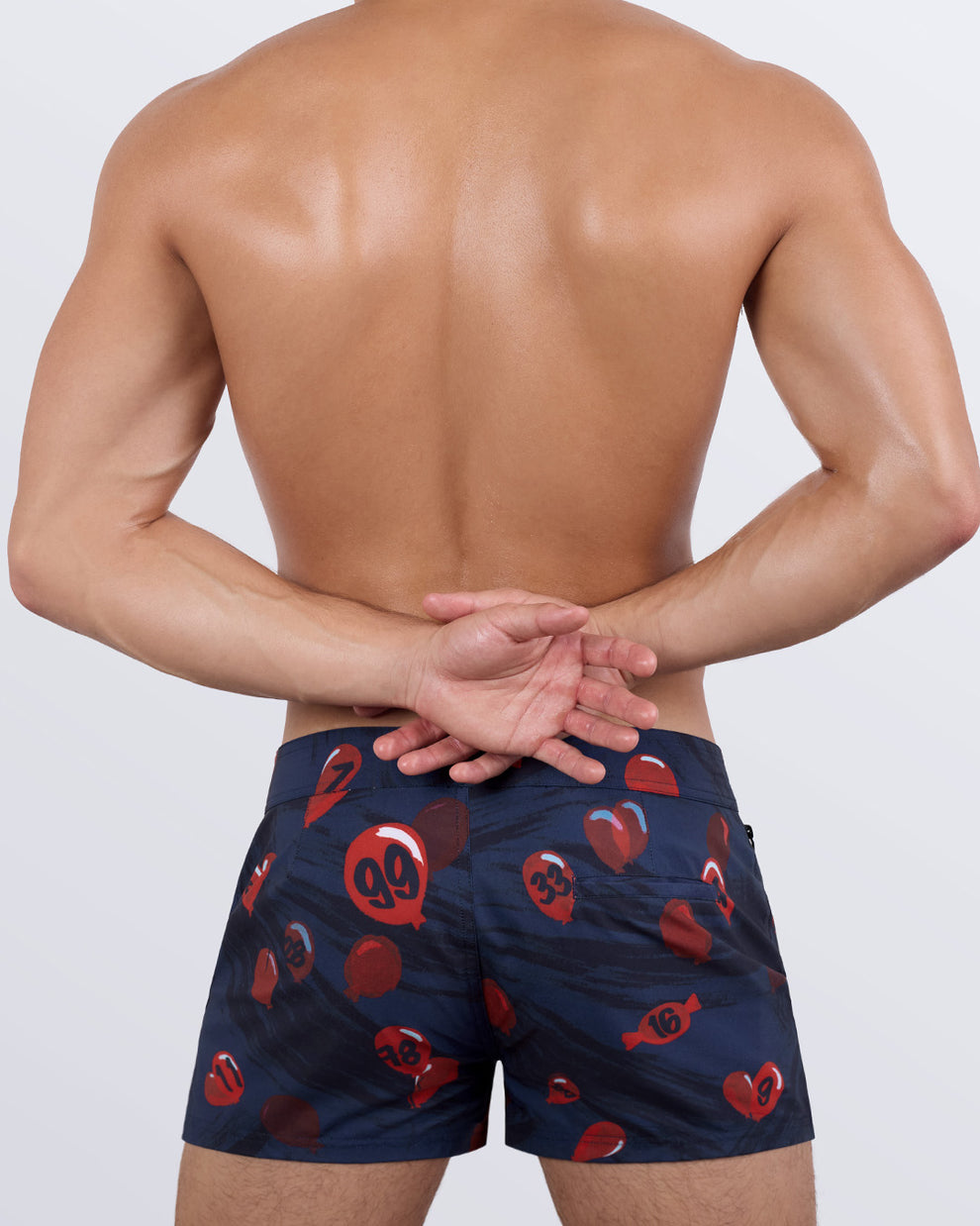 Back view of a male model showcasing the 99 RED BALLOONS Beach Shorts by BANG! Miami. These tailored beach shorts feature a minimalist back pocket design, a seamless waistband, and a comfortable stretch fabric for unrestricted movement.
