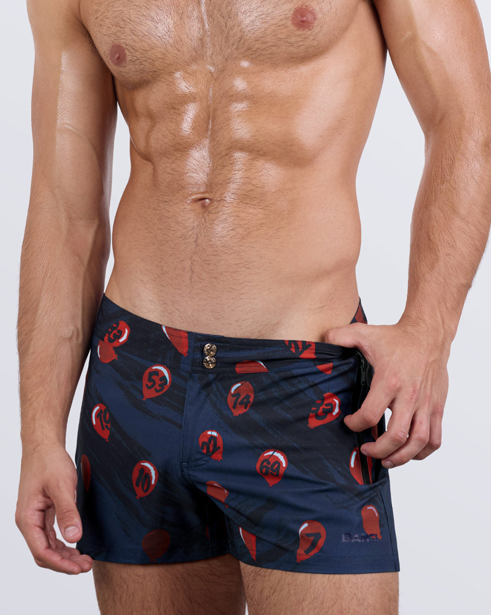 Close-up side view of a male model in the 99 RED BALLOONS Beach Shorts for men by BANG! Miami. The premium-quality shorts feature a tapered leg fit, waterproof metallic zip pockets for secure storage, and a four-way stretch fabric that offers flexibility and comfort.