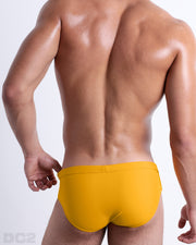 Back view of male model wearing the AMBER SAND beach briefs for men by BANG! Miami in a solid sunny yellow color.