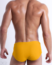 Back view of male model wearing the AMBER SAND beach Brazilian Sunga swimwear for men by BANG! Miami in a solid dark yellow color.