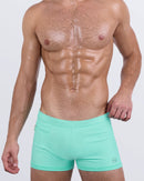 Model wearing AQUA LITE men’s swim trunks in a vibrant seafoam green. These body-contouring trunks feature a sleek, square-cut silhouette and a minimalist front design that blends sporty functionality with elevated poolside style.