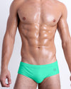 DC2 AQUA GLOW — model wearing Aqua Glow Swim Brief, featuring a vibrant neon green hue in a low-rise, form-fitting silhouette.