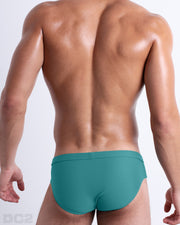 Back view of male model wearing the ATLANTIS TEAL beach briefs for men by BANG! Miami in a solid dark aqua color.