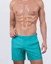 A male model wearing the ATLANTIS - Tailored Shorts by DC2 Miami. These premium shorts feature a vibrant turquoise shade with a sleek, tailored cut and adjustable side buckles for a refined fit.