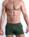 Male model wearing the ALPHA GREEN men’s swim shorts in army green color by the Bang! brand of men's beachwear from Miami.
