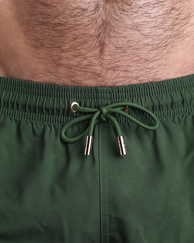 Close-up view of the ALPHA GREEN men’s summer shorts, showing green cord with custom branded golden cord ends, and matching custom eyelet trims in gold.