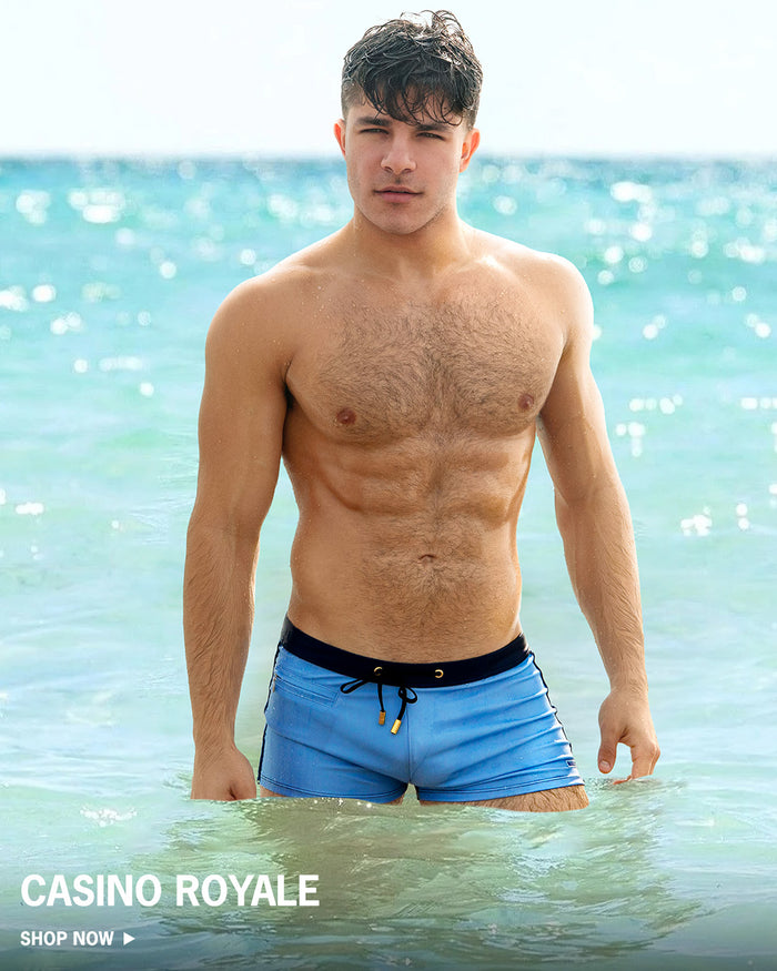 Man wearing blue swim shorts standing in water with 'Casino Royale' branding.