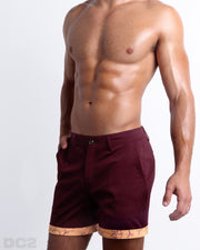 Side view of stretchy men's shorts in BEAU BERRY a dark red color with with two front pockets and custom engraved button front closure with zip fly from DC2. 