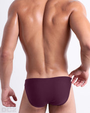 Back view of male model wearing the BERRY GOOD beach mini-briefs for men by BANG! Miami in a solid red wine color.