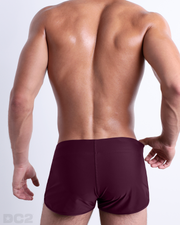 Back view of male model wearing the BERRY GOOD beach Swim Shorts for men by BANG! Miami in a solid red wine color.