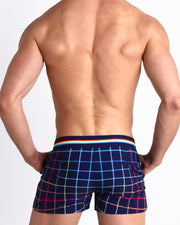 Back view of male model wearing the BJORN THIS WAY (DARK) beach shorts for men by BANG! Miami in navy blue with multi color stripes in red and navy blue.